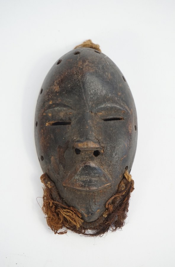 Petit masque DAN figurant un visage. Bois sculpté patiné, fibres végétales. XXe siècle. Côte d'Ivoire.